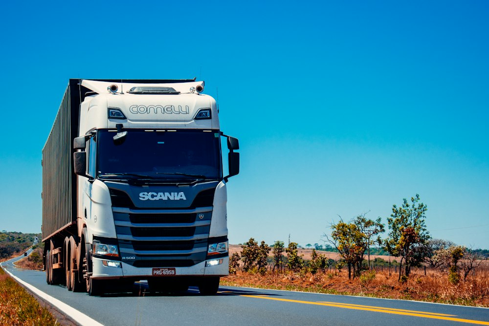 A white freight truck driving along a country road